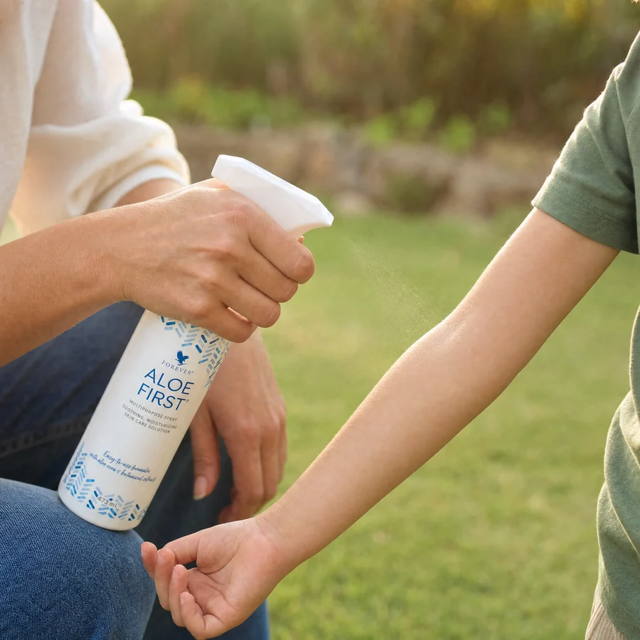 Mamă pulverizând Aloe First pe brațul copilului, în grădină, după joacă